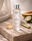 Aura Toning Mist bottle on a stone surface with a lime, papaya, and citrine crystal in the background