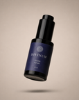 A floating bottle of Divinum Aurelia Serum, featuring a dark purple label and a black dropper cap, set against a solid beige background with a soft shadow underneath.