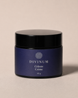 A 50g jar of Divinum Celeste Crème cosmetic cream, featuring a deep purple label and a black lid, set against a warm beige background.