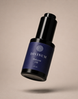 A bottle of Divinum Halcyon Oil floating against a solid beige background. The bottle is dark violet with a black cap and features the brand name 'DIVINUM' and product name 'Halcyon Oil' printed in stone on the label.