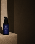 A dark violet bottle of Divinum Mira Cleanser with a black pump dispenser, placed on a textured stone pedestal in dramatic, low-key lighting.