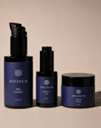 Three Divinum skincare products in dark violet and black packaging, including a pump bottle of Mira Cleanser, a dropper bottle of Halcyon Oil, and a jar of Celeste Creme, arranged on a warm beige background.