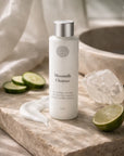 Moonmilk Cleanser bottle with lime, cucumbers, and selenite crystal on a wooden surface