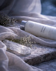 Moonmilk Cleanser bottle on a stone surface with dried flowers and a selenite crystal.