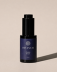 A 30 ml bottle of Divinum Aurelia Serum, featuring a dark purple label and a black dropper cap, set against a warm beige background with a soft shadow.