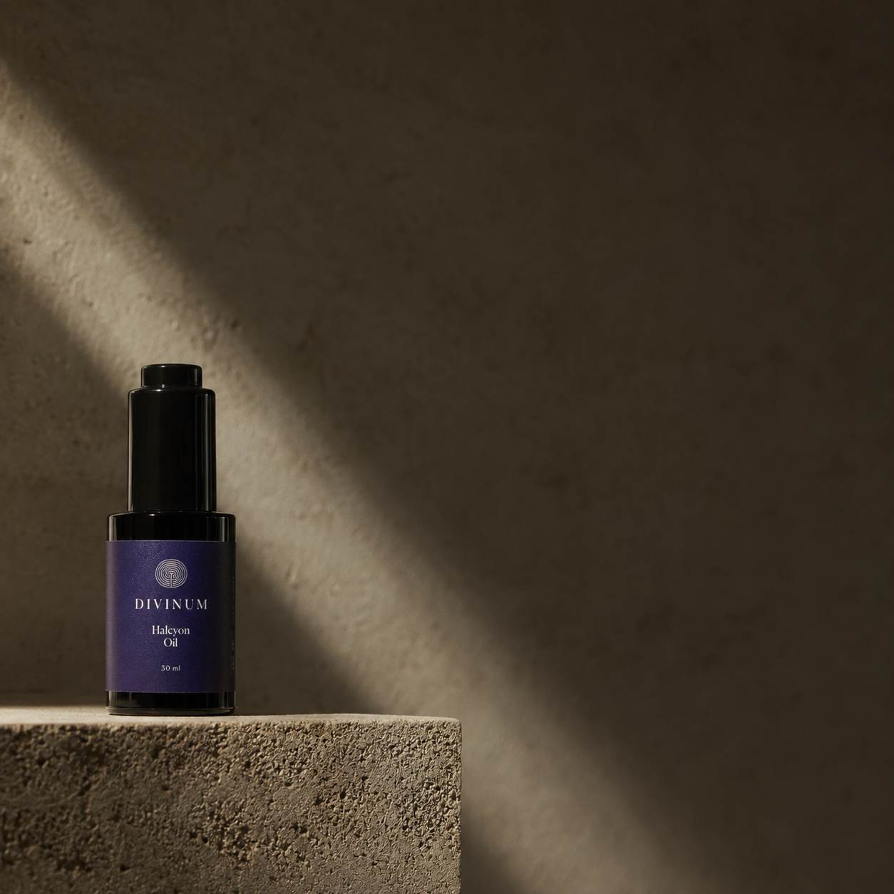 A small violet bottle with a dark purple label reading Divinum Halcyon Oil, placed on a textured stone pedestal in dramatic side lighting against a dark stone wall.