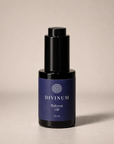 A 30 ml bottle of Divinum Halcyon Oil, featuring a dark purple label and a black dropper cap, set against a neutral beige background.