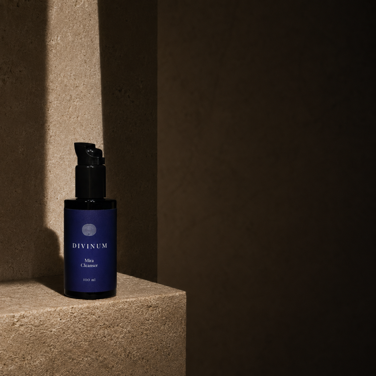 A dark violet bottle of Divinum Mira Cleanser with a black pump dispenser, placed on a textured stone pedestal in dramatic, low-key lighting.