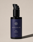 A 100 ml bottle of Divinum Mira Cleanser, featuring a dark purple label and a violet pump dispenser, set against a warm beige background with a soft shadow.
