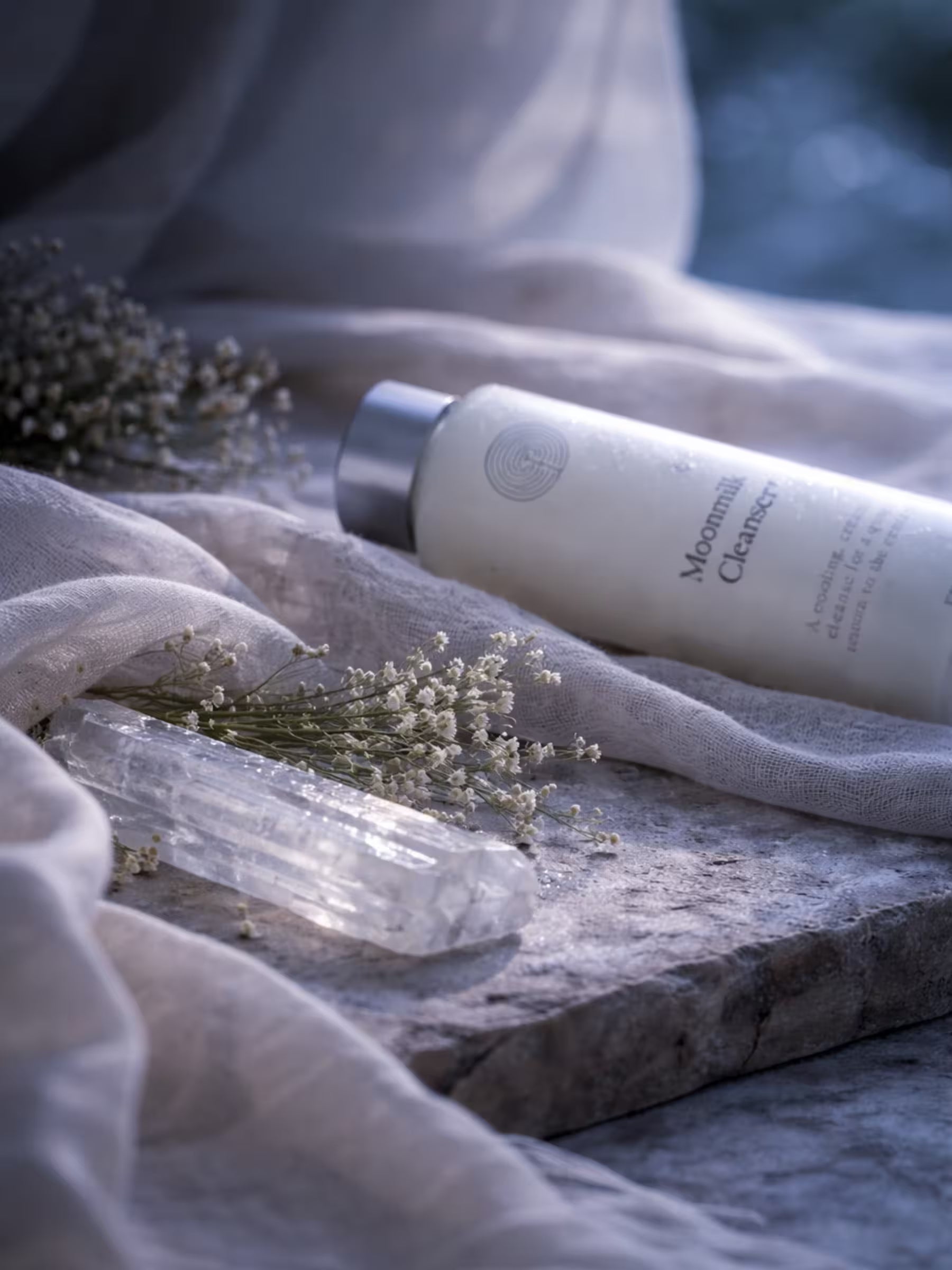 Moonmilk Cleanser bottle on a textured surface with flowers and selenite