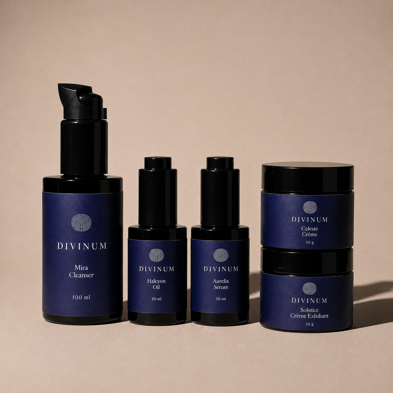 Five Divinum skincare bottles and jars arranged on a warm beige studio background. The set includes a pump bottle of Mira Cleanser, two small bottles of Halcyon Oil and Aurelia Serum, and two stacked jars of Celeste Creme and Solstice Creme Exfoliant.