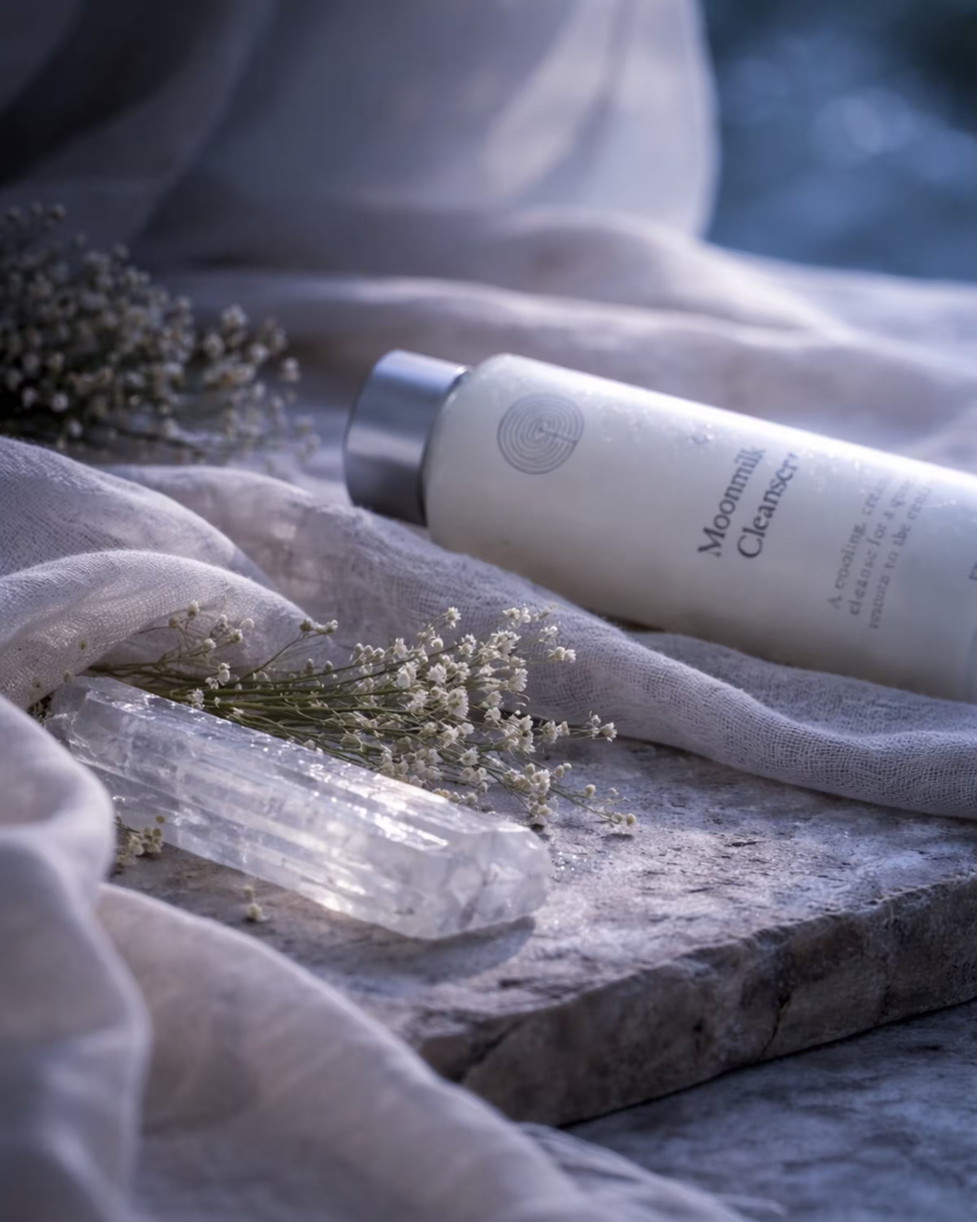 Moonmilk Cleanser bottle on a stone surface with dried flowers and a selenite crystal.