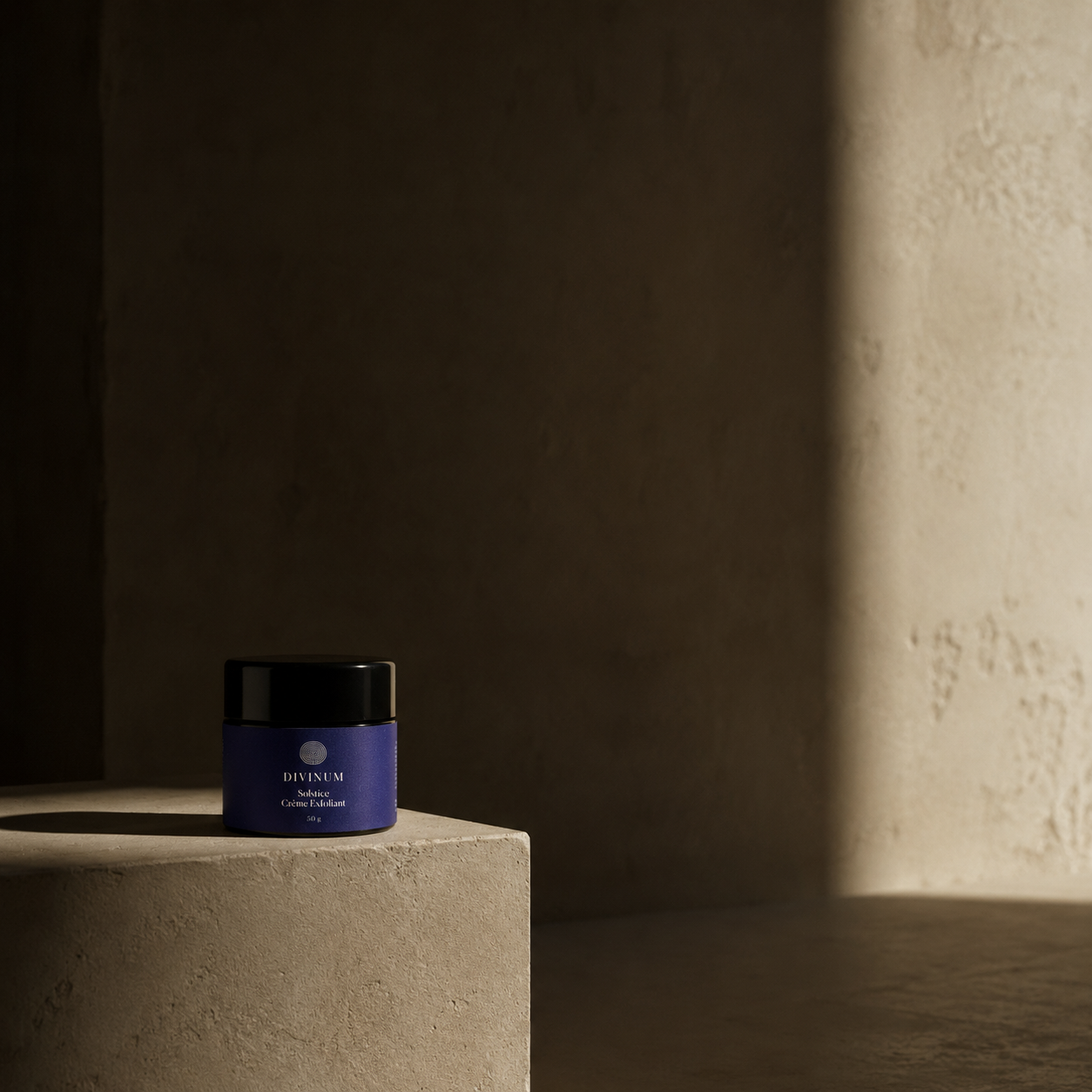 A small violet glass cosmetic jar with a black lid sits on a textured beige pedestal in a dimly lit studio setting with a warm spotlight on the right.