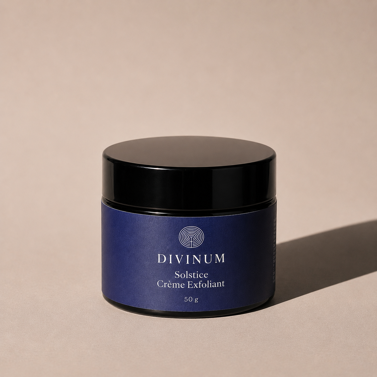 A 50g jar of Divinum Solstice Crème Exfoliant, featuring a deep purple label and a black lid, set against a warm beige background with a soft shadow.